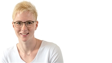 Eine blonde Frau mit kurzen Haaren und Brille lächelt in die Kamera.