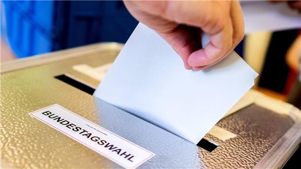 Eine Person schiebt den Wahlzettel in die Urne.