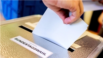 Eine Person schiebt den Wahlzettel in die Urne.