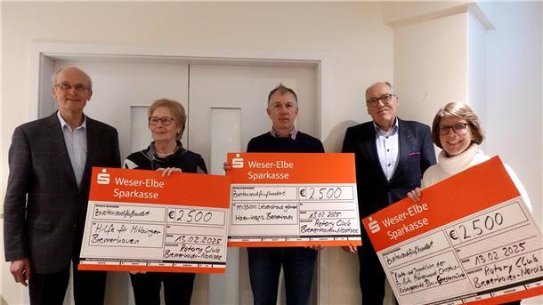 Drei Männer und zwei Frauen stehen nebeneinander und halten drei Riesenschecks in den Händen.