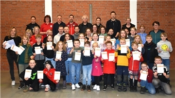 Erwachsene und Kinder stehen in einer Gruppe. In den Händen halten sie Urkunden.