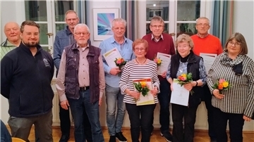 Drei Frauen und sieben Männer stehen in einer Gruppe zusammen. Fünf Personen davon halten eine Urkunde und Blumen in der Hand.