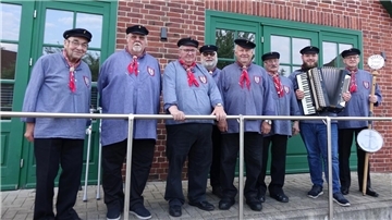 Das Foto zeigt acht Mitglieder eines Shanty-Chores in traditioneller Tracht. Der zweite Herr von rechts hält ein Akkordeon in den Händen.