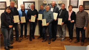 Männer und Fraauen mit Urkunden in der Hand stehen nebeneinander vor einer Wand.