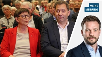 Eine Frau in roter Jacke sitzt neben einem Mann im Anzug. 