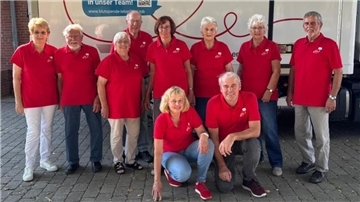 Gruppenfoto von zehn ehrenamtlichen Helferinnen und Helfern des DRK-Blutspendeteams Sievern in roten Poloshirts vor einem Blutspendewagen.