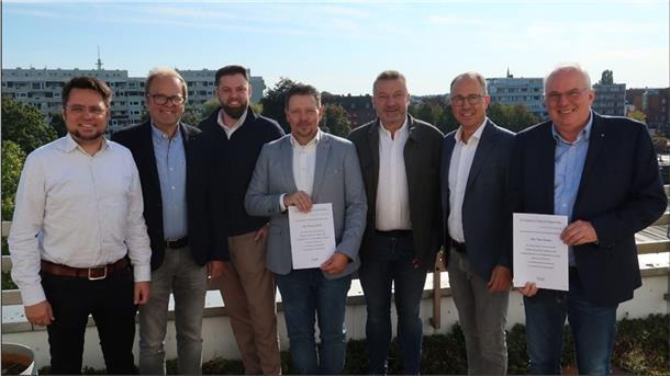 Gruppenbild mit sieben Männern. Zwei von ihnen halten eine Urkunde in den Händen.