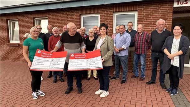 2.800 Euro für Wremens Jugend: Aale machen’s möglich Gruppenfoto von einer Spendenübergabe. Im Vordergrund halten drei Personen zwei symbolische Spendenschecks in die Höhe.