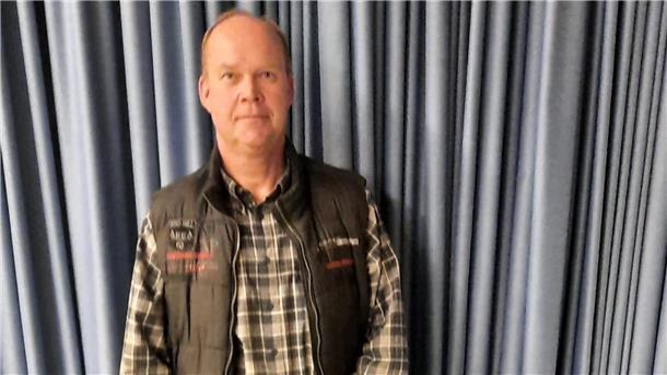 Ein Mann steht vor einem grauen Vorhang.