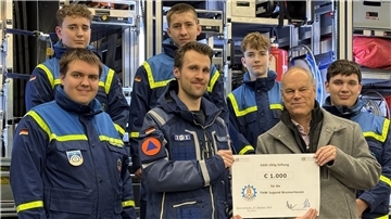 Zwei Männer aus einer Gruppe halten einen großen Scheck.