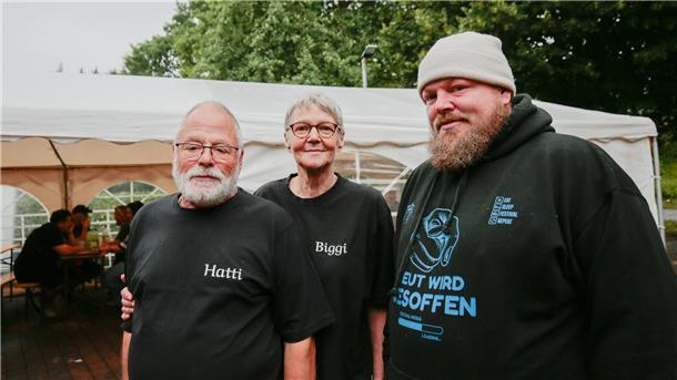 Drei Personen im schwarzen Oberteil vor weißem Pavillon