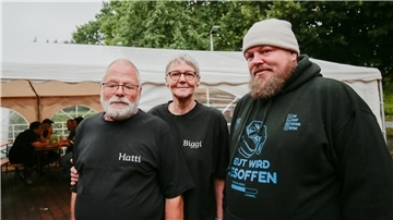 Drei Personen im schwarzen Oberteil vor weißem Pavillon