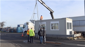 Männer stehen vor einem Baucontainer.