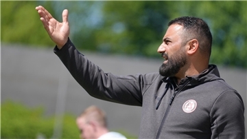 Ein Fußballtrainer gestikuliert am Spielfeldrand.