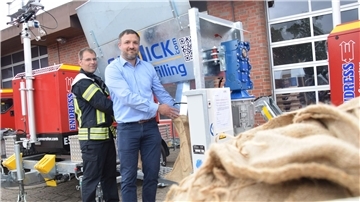 Zwei Männer stehen an einer Sandsackbefüllmaschine.