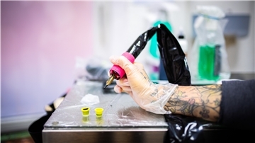 Eine Tätowiererin hält eine Tattoonadel in der Hand.