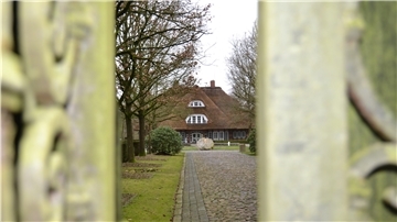 Durch ein Gartentor sieht man ein Herrenhaus.
