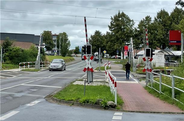 Ein Straße, auf der ein Auto fährt. Bahnschranken sind zu sehen, ebenso wie ein Fußgänger.