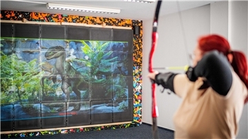 Eine Frau schießt mit einem Bogen auf eine Leinwand mit einem Dinosaurier 