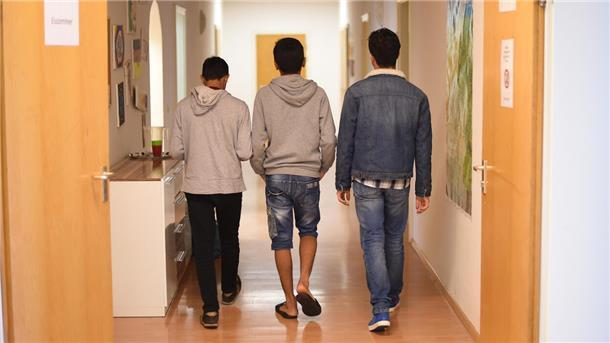 Rückansicht von drei jugendlichen Flüchtlingen auf einem Flur.