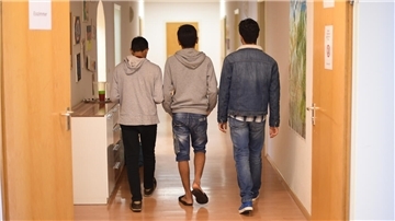 Rückansicht von drei jugendlichen Flüchtlingen auf einem Flur.