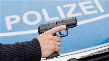 in Polizist posiert mit seiner Dienstwaffe vor einem Polizeifahrzeug.