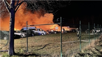 Auf einer eingezäunten Rasenfläche stehen brennende Fahrzeuge kurz nach Eintreffen der Feuerwehr.
