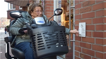 Ältere Dame sitzt auf einem City-Roller und klingelt bei der Buchhandlung Bestenbostel in Nordenham. 