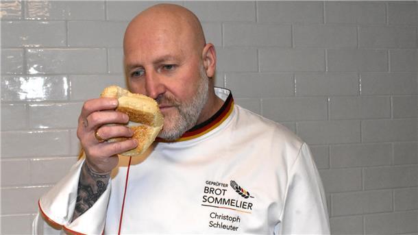 Ein Mann mit einer Glatze und einer weißen Jacke riecht an einem Brot.