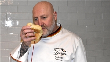 Ein Mann mit einer Glatze und einer weißen Jacke riecht an einem Brot.