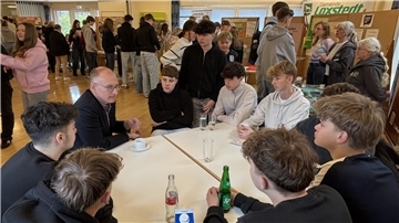 Bürgermeister Detlef Wellbrock sitzt mit einer Gruppe Jugendlicher an einem runden Tisch im Bürgersaal und spricht mit ihnen, während im Hintergrund weitere Jugendliche an Infoständen und Gesprächsinseln aktiv sind.