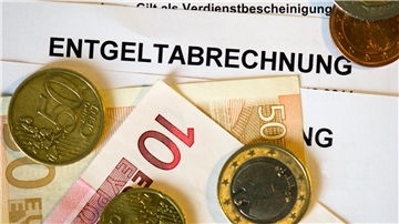 Auf Lohn- und Gehaltsabrechnungen (Entgeltabrechnungen) liegen Euromünzen und Eurogeldscheine.