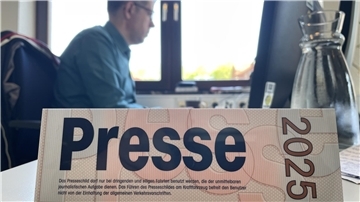 Ein Presse-Schild im Vordergrund. Dahinter ein Journalist bei der Arbeit.  