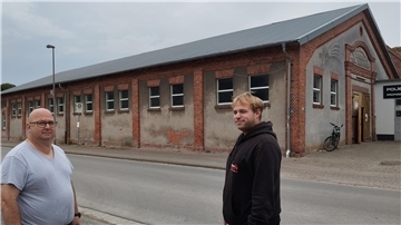 Es sind der Bürgervereins-Vorsitzende und dessen Sohn zu sehen, sowie die Alte Reithalle im Hintergrund, die mit Solarpanelen bestückt werden könnte. 