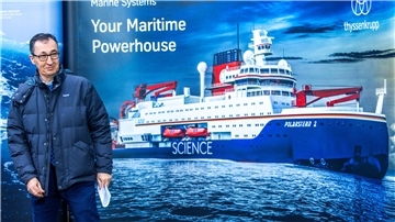 Ein Mann steht vor einem Plakat mit einem abgebildeten Schiff.