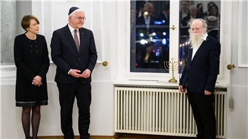 Bundespräsident Frank-Walter Steinmeier und seine Frau Elke Büdenbender sowie Yehuda Mansbach (r), der Enkel von Rabbiner Arthur Posner, bei der gemeinsamen Chanukka-Feier im Schloss Bellevue. Auf der Fensterbank steht der Chanukka-Leuchter der Familie Posner.