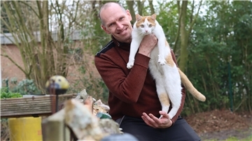 Christian Gerdon hält seinen Kater Tiger im Arm und blickt in die Kamera.