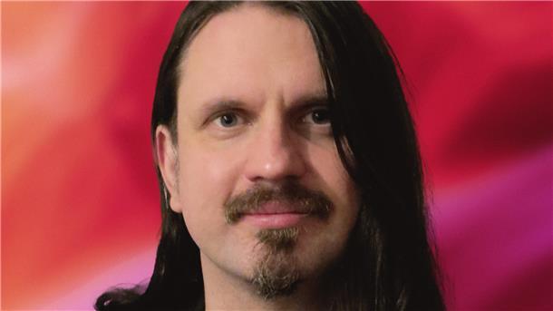 Mann mit langen Haaren und Bart vor einem roten Hintergund.