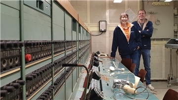 Ein Mann und eine Frau stehen in einem Bunker an einer Telefonanlage.