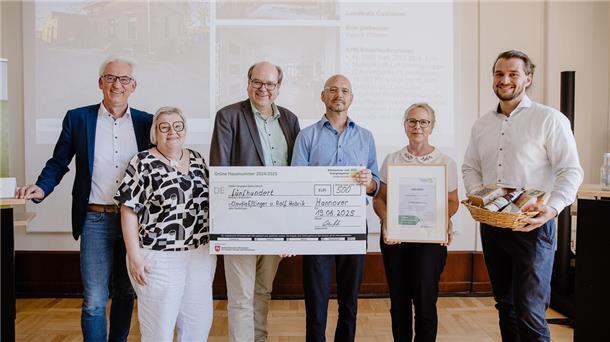 Gruppenfoto bei der Preisverleihung „Grüne Hausnummer 2024/2025“: Claudia Eßlinger und Ralf Habrik aus Nordleda halten einen großen Scheck über 500 Euro, eine Urkunde und einen Geschenkkorb in den Händen, flankiert von Gratulanten.