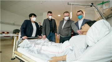 Vier Menschen stehen an einem Krankenhausbett und sehe ich sich eine digitalisierte Patientenpuppe an.