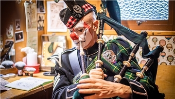 Ein geschminkter Clown sitzt vor einem Spiegel und spielt Dudelsack.