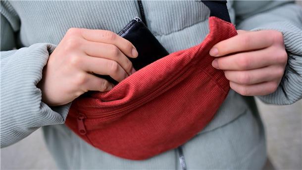 Cord lässt sich im Alltag wieder öfter antreffen; Eine Frau trägt eine Jacke und eine Brusttasche aus Cord und steckt ihr Portemonnaie in die Tasche. (Foto: Illustration)