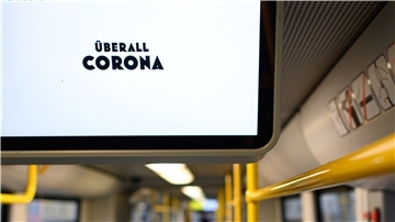 Auf einem Bildschirm in der Bahn steht die Aufschrift "Überall Corona".