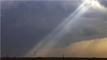 Das Sonnenlicht fällt durch die Sturmwolken auf eine Windturbine