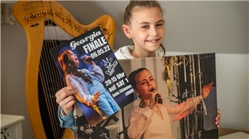 Dank des „Community-Tickets“ steht Georgia im Finale der Gesangsshow „The Voice Kids“. Damit möglichst viele anrufen, werden Plakate in der Stadt verteilt.