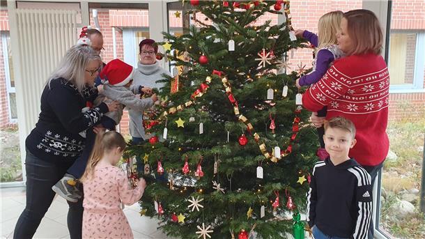 Erwachsene und Kinder hängen Schmuck an einen Weihnachtsbaum.