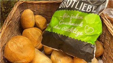 Eine gefüllte Brötchentüte liegt in einem gefüllten Brötchenkorb.
