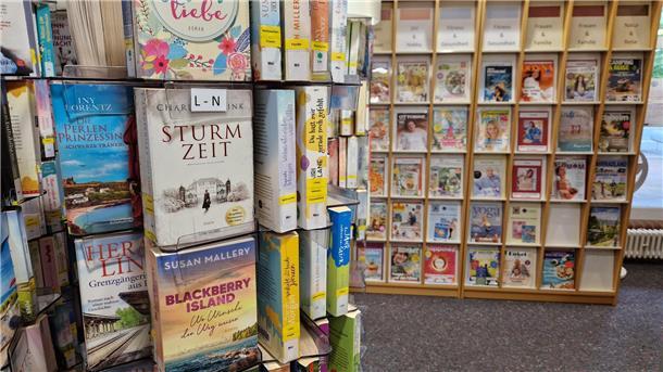Ein Bücherständer im Vordergrund und ein Regal mit Magazinen im Hintergrund.