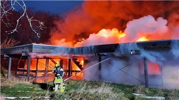 Brennendes Gebäude mit lodernden Flammen, zwei Feuerwehrleute versuchen, das Feuer zu löschen